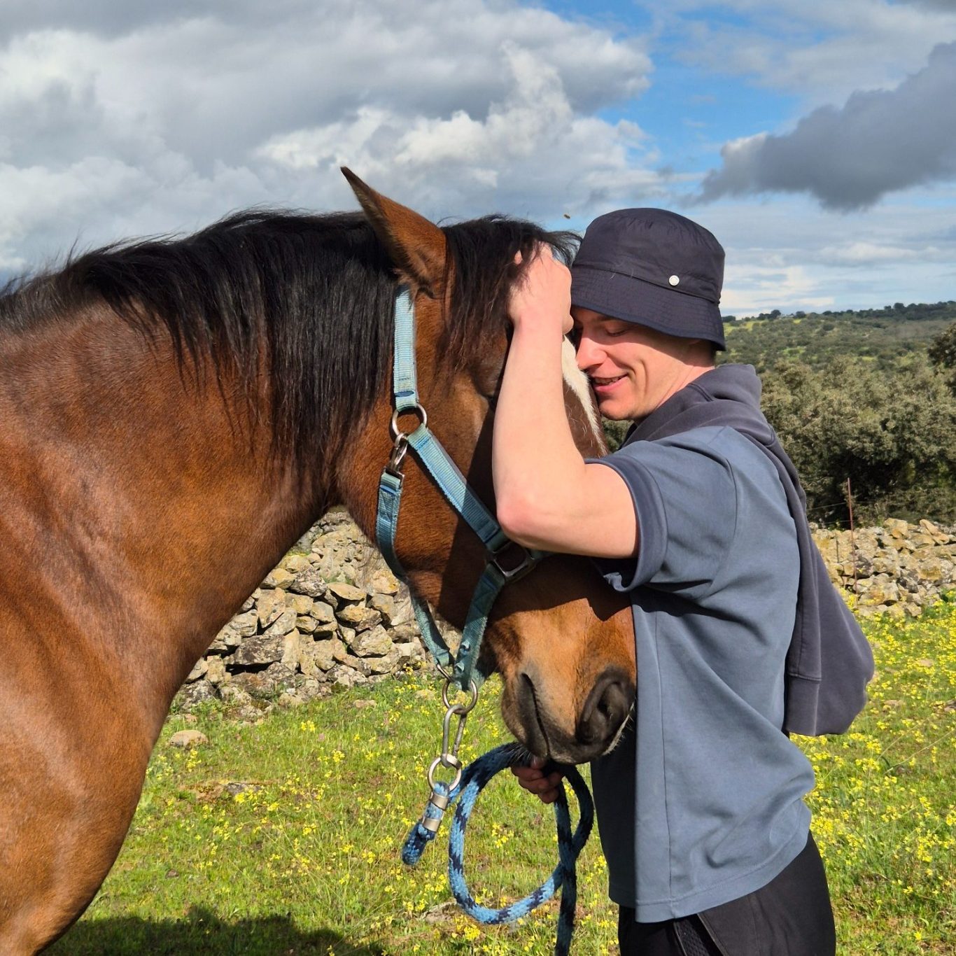 Respeto animal Persona abrazando un caballo en un paisaje campestre con cielo nublado.